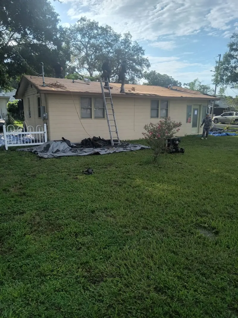 Customer photo from a Tampa re-roof: crew on the eave, ladder up, tarps on the lawn