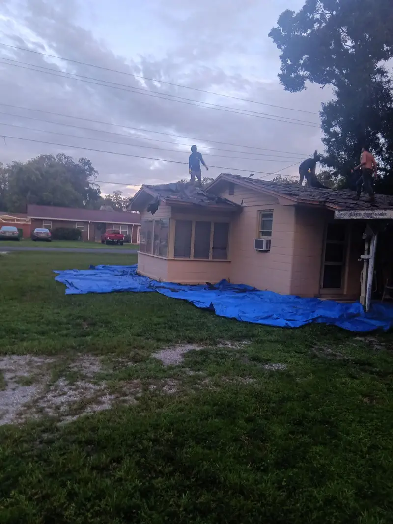 Customer photo from a Tampa re-roof: roofers on the edge, blue tarp on the lawn at dusk