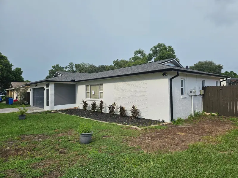 Customer photo: white brick ranch home with a new dark gray shingle roof and black gutters
