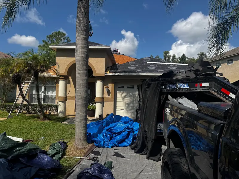 Tear-off in progress with blue tarps on the lawn and a palm in front of the house