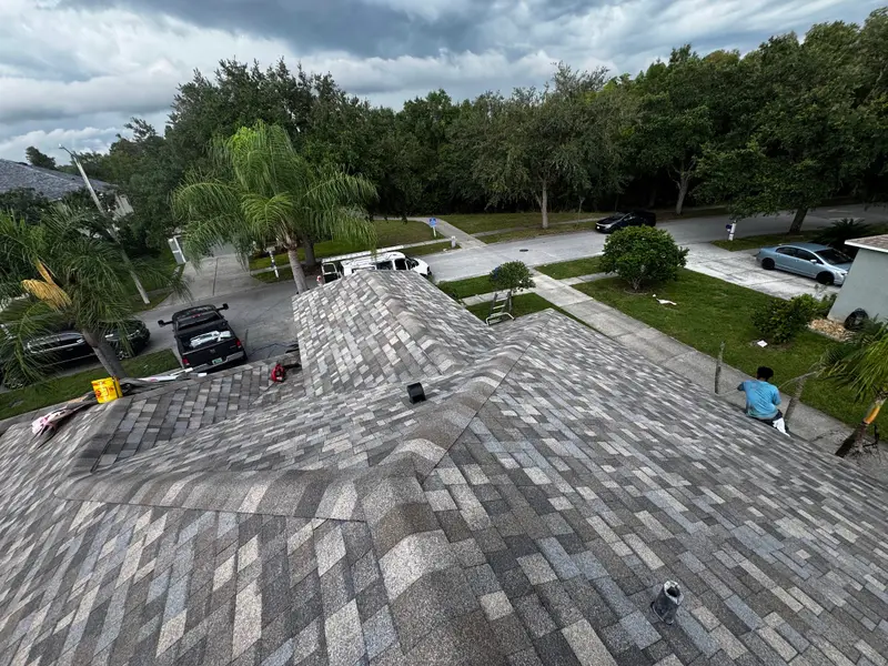New hip roof of gray architectural shingles seen from the ridge, neighborhood street below