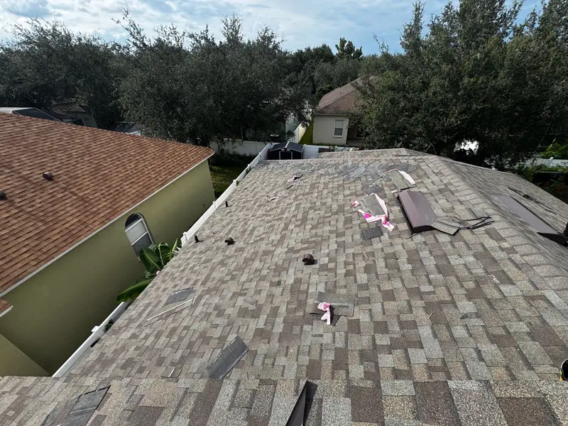 Hip roof mid-install: new gray shingles laid on one side, shingle wrappers on the deck