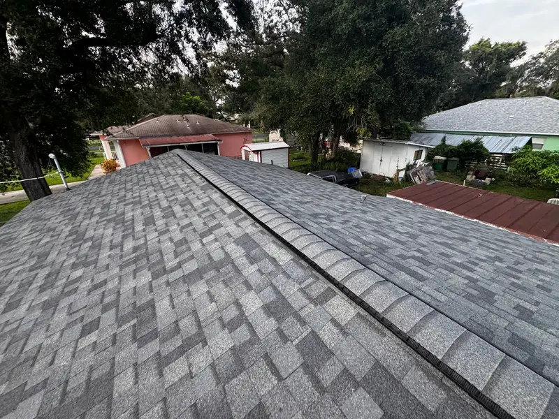 Finished gray shingle hip and ridge with neighboring roofs and trees around it