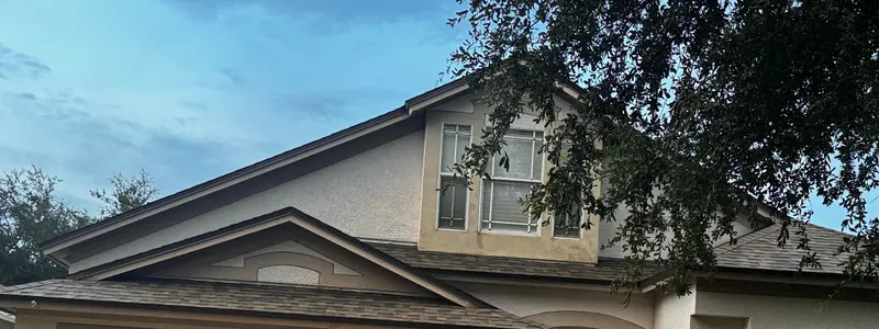 Two-story stucco home with a dark gray shingle roof under live oaks