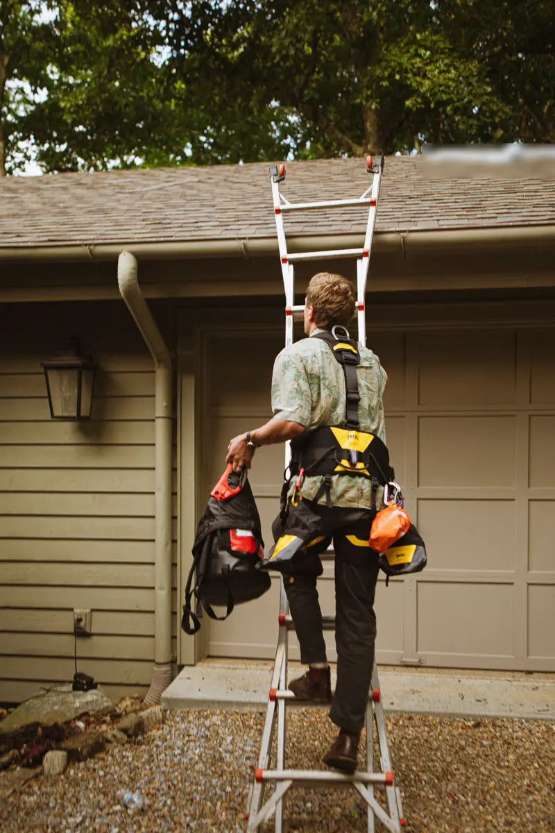 Roofer climbing a ladder to the roof edge, seen from behind