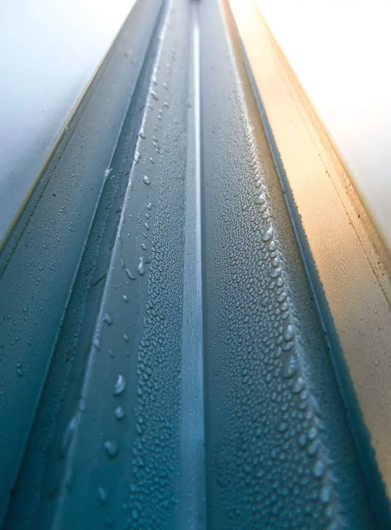 Close-up of a standing-seam metal roof rib with water beads