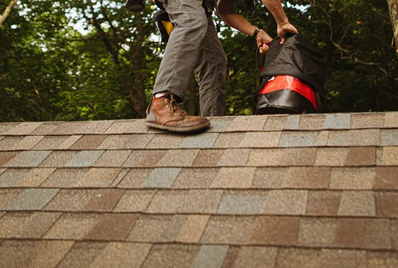 Roofer working on a shingle roof under the trees